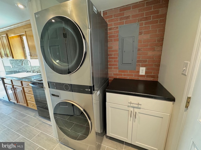 washroom featuring cabinets, stacked washer and dryer, electric panel, sink, and brick wall