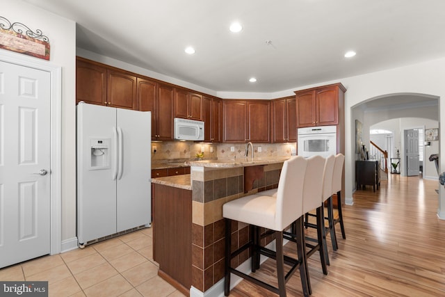 kitchen with light wood-type flooring, light stone counters, decorative backsplash, a kitchen breakfast bar, and white appliances