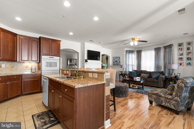 kitchen featuring ceiling fan, sink, white appliances, a center island with sink, and light hardwood / wood-style flooring