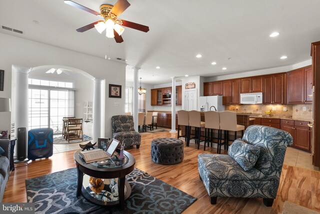 dining space with ceiling fan with notable chandelier, light wood-type flooring, crown molding, and ornate columns