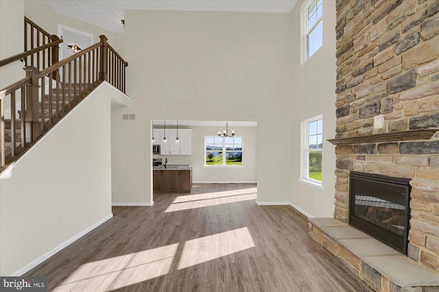 unfurnished living room with sink, hardwood / wood-style flooring, a notable chandelier, a fireplace, and a high ceiling