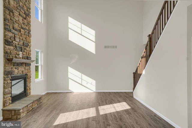 unfurnished living room with a high ceiling, hardwood / wood-style floors, and a stone fireplace