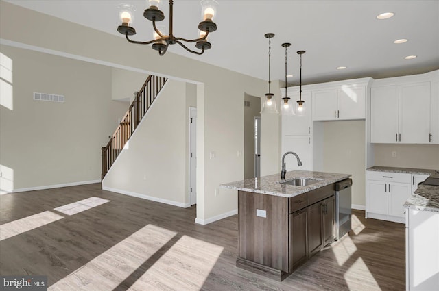 kitchen with dark hardwood / wood-style floors, stainless steel dishwasher, a kitchen island with sink, and light stone counters