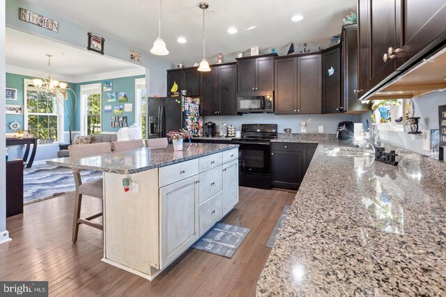 kitchen with light wood-type flooring, black appliances, dark stone counters, a kitchen breakfast bar, and a kitchen island