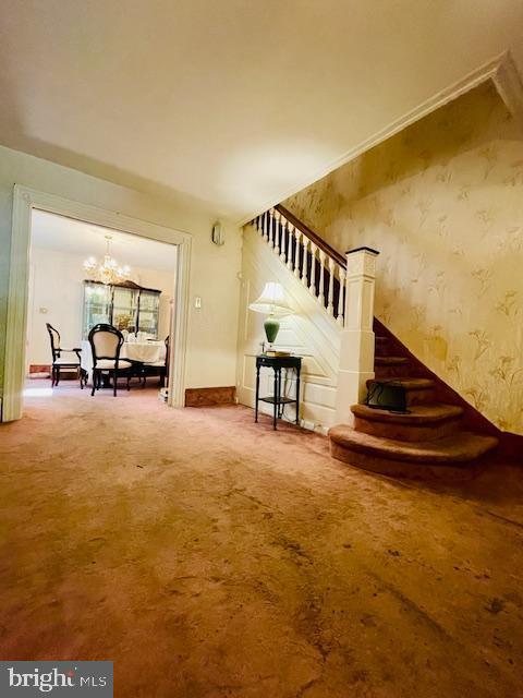 staircase with an inviting chandelier and carpet floors