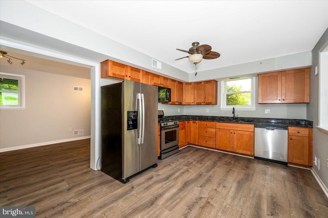 kitchen with appliances with stainless steel finishes, dark stone countertops, ceiling fan, dark hardwood / wood-style floors, and sink