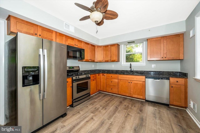 kitchen featuring ceiling fan, sink, light hardwood / wood-style flooring, stainless steel appliances, and dark stone countertops