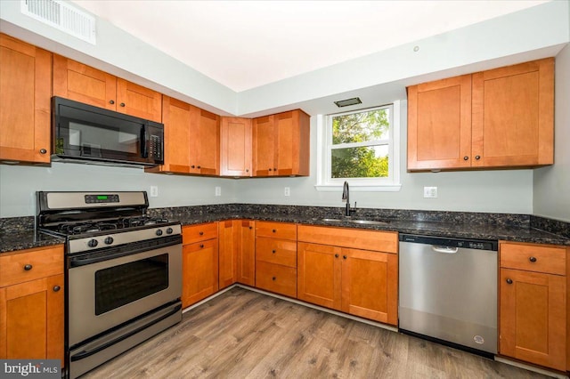 kitchen with appliances with stainless steel finishes, dark stone counters, light wood-type flooring, and sink