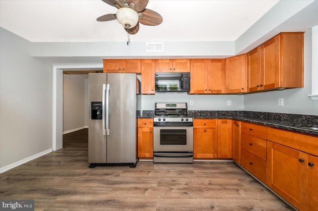 kitchen featuring stainless steel appliances, dark stone countertops, ceiling fan, and dark wood-type flooring