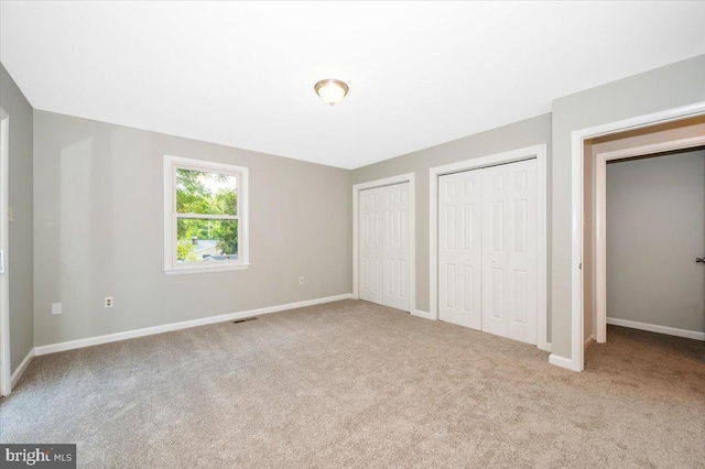 unfurnished bedroom featuring two closets and light colored carpet