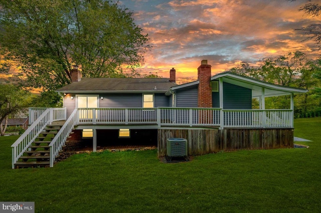 back house at dusk with central AC unit, a wooden deck, and a lawn