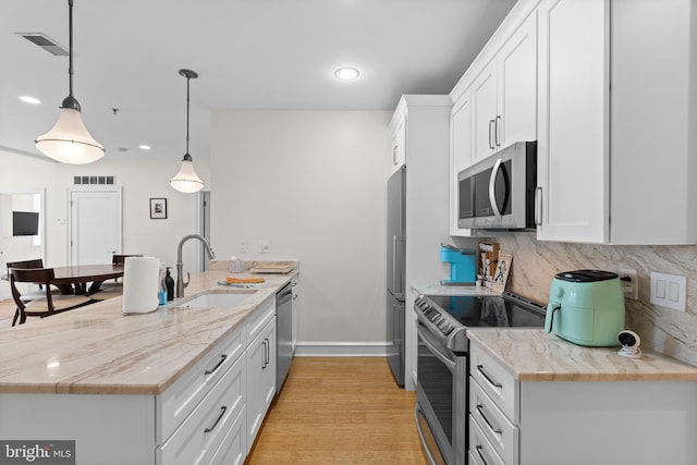 kitchen featuring appliances with stainless steel finishes, white cabinets, pendant lighting, light wood-type flooring, and sink