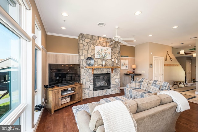 living room featuring crown molding, a stone fireplace, dark wood-type flooring, and ceiling fan