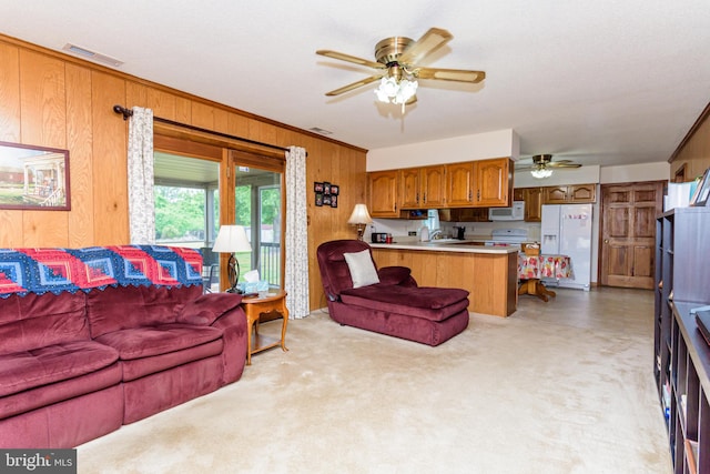 carpeted living room with ceiling fan, sink, wood walls, and ornamental molding