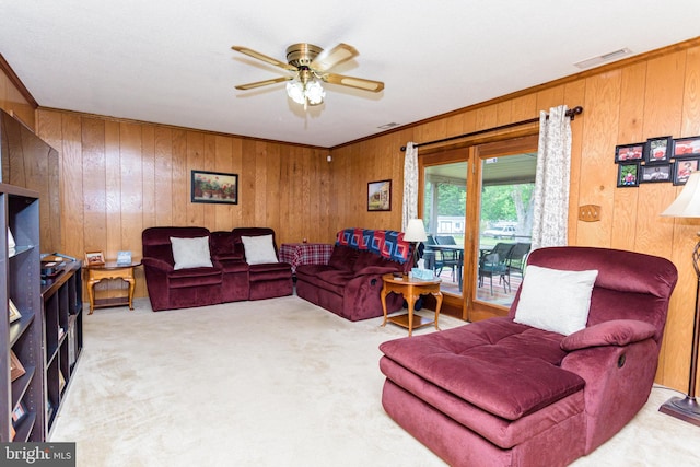 carpeted living room with ceiling fan, wooden walls, and crown molding