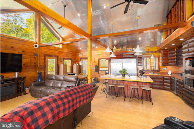 living room featuring light hardwood / wood-style floors, a fireplace, high vaulted ceiling, wooden walls, and ceiling fan