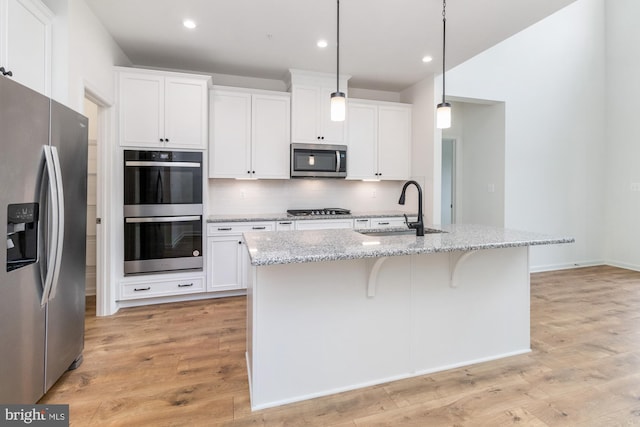 kitchen featuring pendant lighting, an island with sink, stainless steel appliances, and light hardwood / wood-style flooring