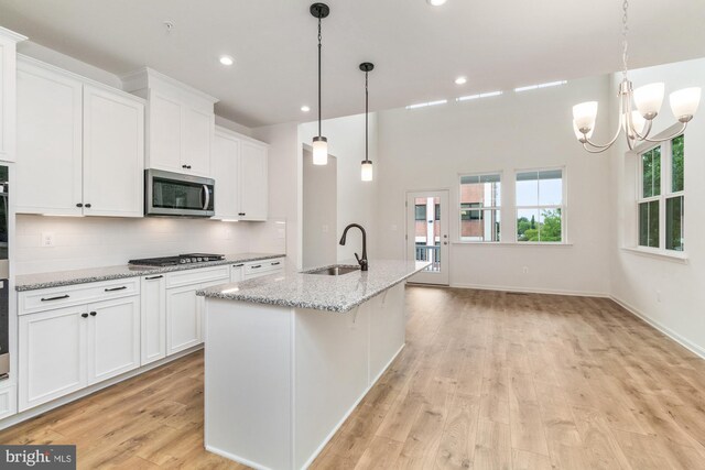 kitchen with white cabinetry, stainless steel appliances, light wood-type flooring, a center island with sink, and sink