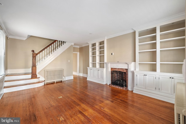 unfurnished living room featuring hardwood / wood-style floors, built in shelves, ornamental molding, a fireplace, and radiator heating unit