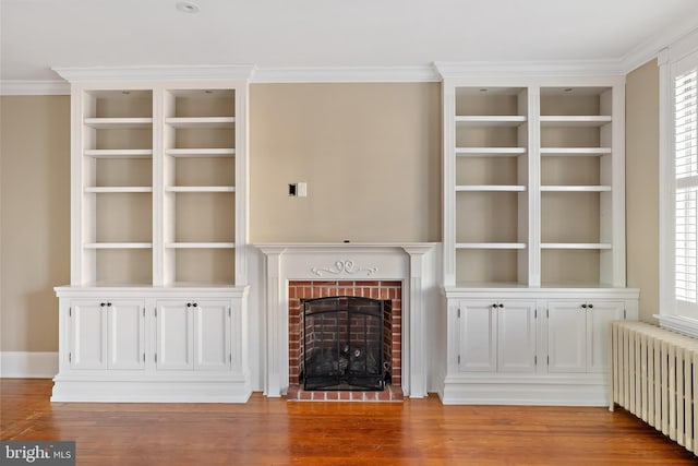 unfurnished living room featuring light hardwood / wood-style floors, crown molding, radiator, and a brick fireplace