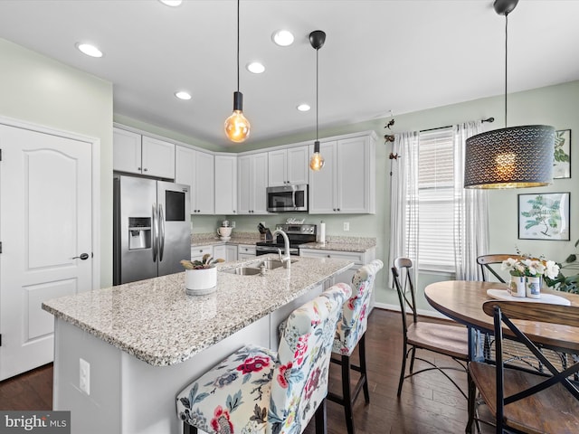 kitchen with decorative light fixtures, a kitchen island with sink, white cabinetry, appliances with stainless steel finishes, and dark hardwood / wood-style flooring