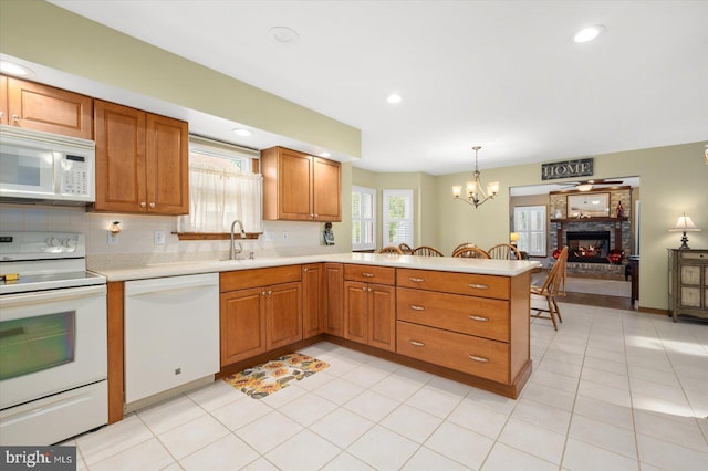 kitchen with kitchen peninsula, an inviting chandelier, a brick fireplace, white appliances, and decorative light fixtures