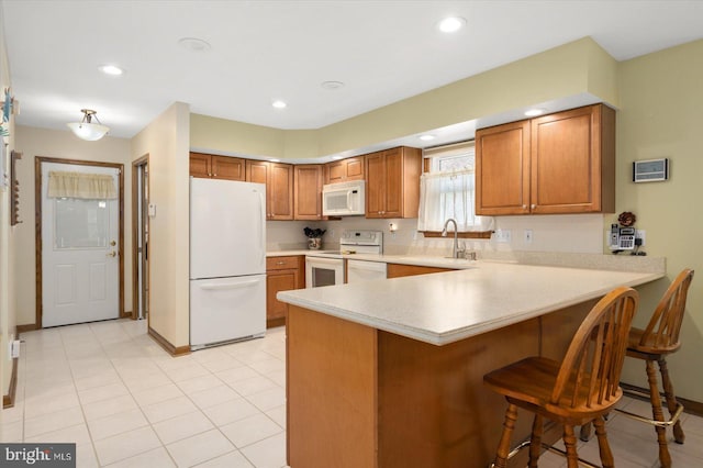 kitchen with light tile patterned flooring, sink, kitchen peninsula, white appliances, and a breakfast bar