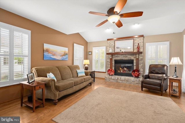 living room featuring ceiling fan, light wood-type flooring, lofted ceiling, and a brick fireplace