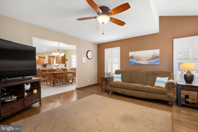 living room with ceiling fan with notable chandelier, light wood-type flooring, and vaulted ceiling