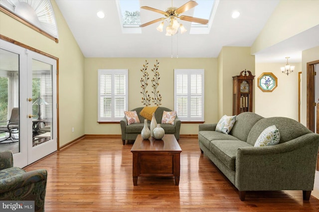 living room with lofted ceiling with skylight, ceiling fan with notable chandelier, and hardwood / wood-style floors