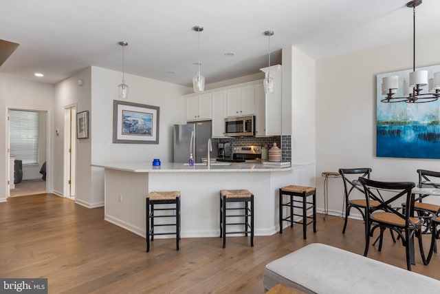 kitchen featuring white cabinetry, stainless steel appliances, kitchen peninsula, dark hardwood / wood-style floors, and a breakfast bar area