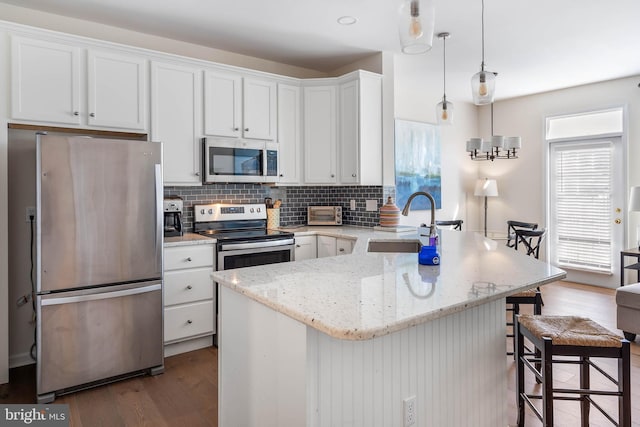 kitchen with white cabinetry, decorative light fixtures, a kitchen breakfast bar, wood-type flooring, and appliances with stainless steel finishes