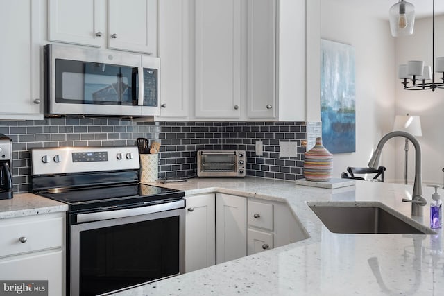 kitchen featuring white cabinets, appliances with stainless steel finishes, light stone countertops, and sink