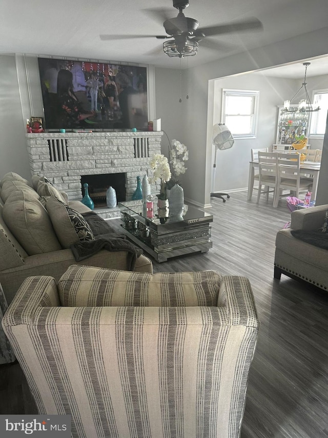 living room featuring a stone fireplace, ceiling fan with notable chandelier, hardwood / wood-style flooring, and a healthy amount of sunlight