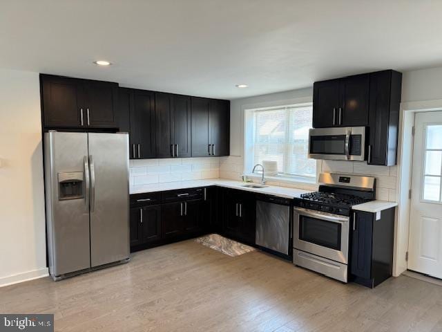 kitchen featuring appliances with stainless steel finishes, backsplash, light wood-type flooring, and sink