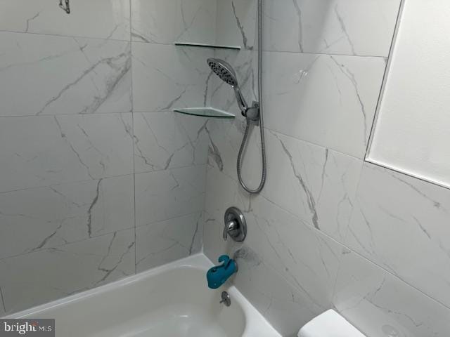 bathroom featuring tiled shower / bath combo and toilet