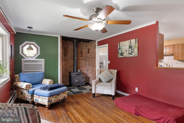 living area featuring a baseboard heating unit, hardwood / wood-style flooring, a wood stove, crown molding, and ceiling fan