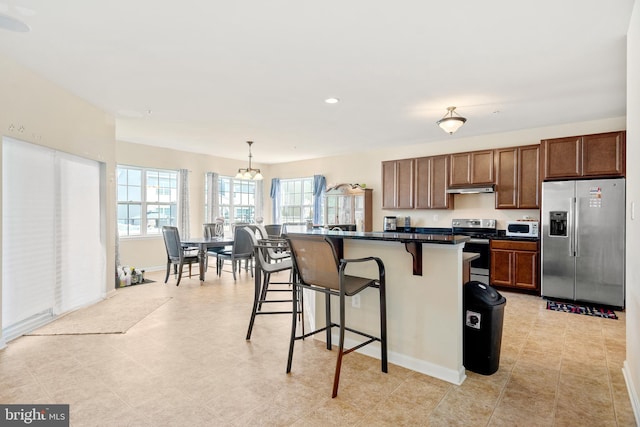 kitchen with a kitchen island, an inviting chandelier, appliances with stainless steel finishes, hanging light fixtures, and a breakfast bar