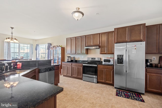 kitchen with appliances with stainless steel finishes, a chandelier, sink, dark stone counters, and pendant lighting