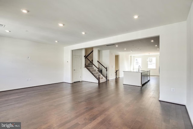 unfurnished living room featuring an inviting chandelier, sink, and dark hardwood / wood-style floors