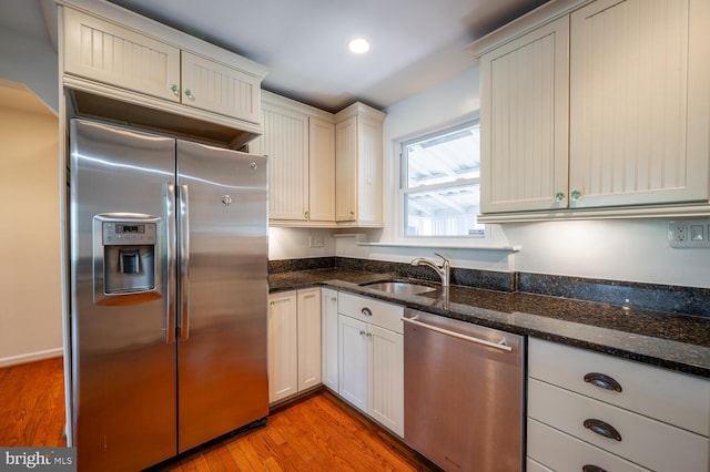 kitchen with white cabinetry, stainless steel appliances, light hardwood / wood-style flooring, dark stone counters, and sink