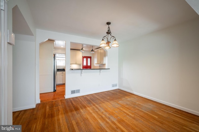 interior space featuring pendant lighting, an inviting chandelier, light hardwood / wood-style floors, and kitchen peninsula