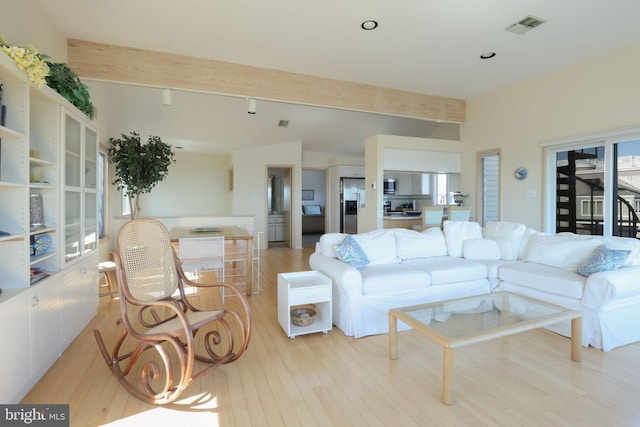 living room with a healthy amount of sunlight, beamed ceiling, and light wood-type flooring