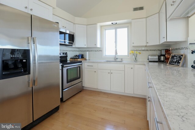 kitchen with white cabinets, light hardwood / wood-style flooring, appliances with stainless steel finishes, sink, and decorative backsplash