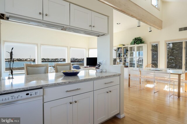 kitchen with light stone countertops, white dishwasher, light hardwood / wood-style floors, white cabinetry, and a towering ceiling