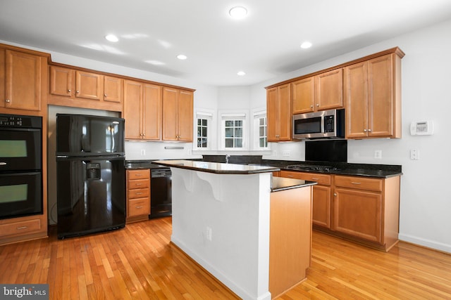 kitchen featuring dark stone countertops, a breakfast bar, a kitchen island, black appliances, and light hardwood / wood-style flooring