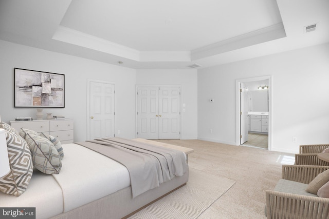 bedroom with a raised ceiling, a closet, light carpet, crown molding, and ensuite bathroom