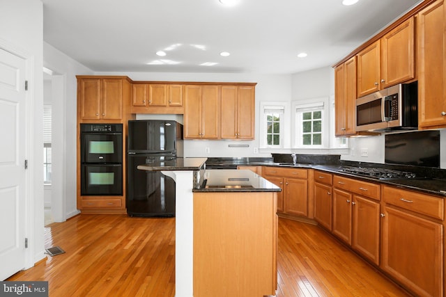 kitchen featuring dark stone countertops, a kitchen island, light wood-type flooring, black appliances, and a kitchen bar