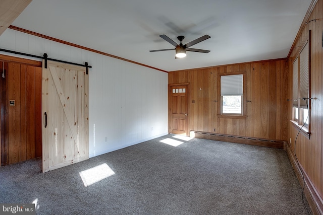 empty room featuring carpet, ceiling fan, a barn door, wood walls, and crown molding