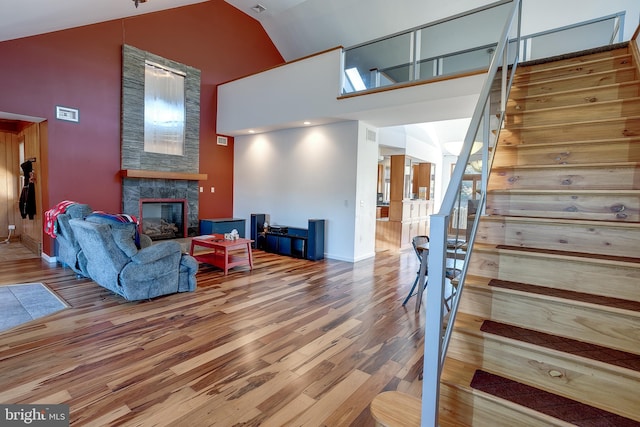 living room with high vaulted ceiling, hardwood / wood-style flooring, and a stone fireplace